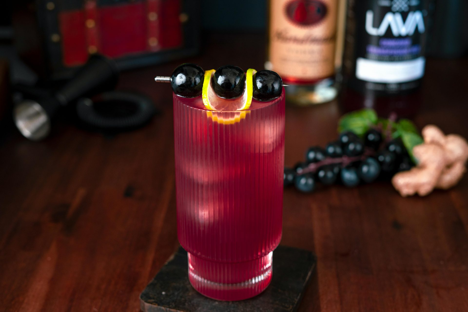 Ein raffinierter roter Cocktail, garniert mit schwarzen Trauben und einer Zitronenscheibe, perfekt für einen stilvollen Abend.