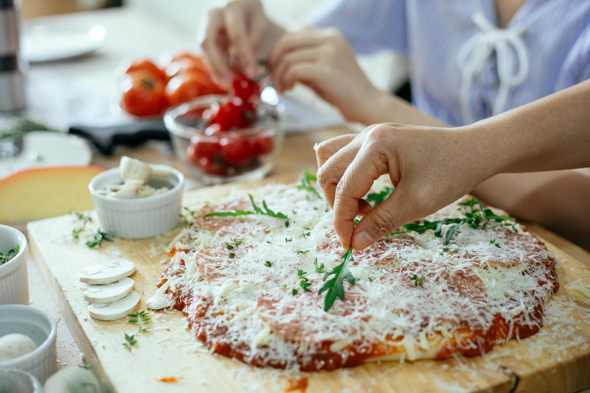 Eine Person fügt in einer Küche einer selbstgemachten Pizza frischen Rucola hinzu.